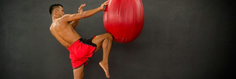 A man in red shorts kicking a red boxing bag