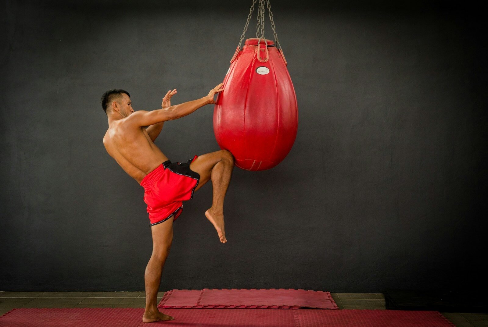 A man in red shorts kicking a red boxing bag