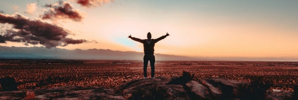 person standing on rock raising both hands